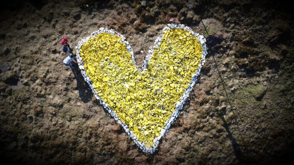 A view from above of a yellow heart made of stones on a hillside.